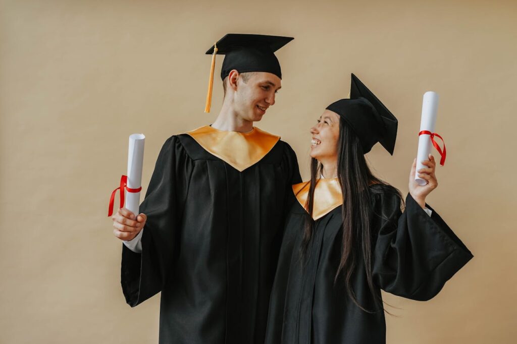 Two happy graduates in caps and gowns celebrating their achievement indoors.